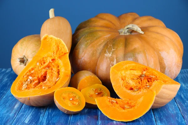 Ripe cut pumpkins on wooden table on blue background — Stock Photo, Image