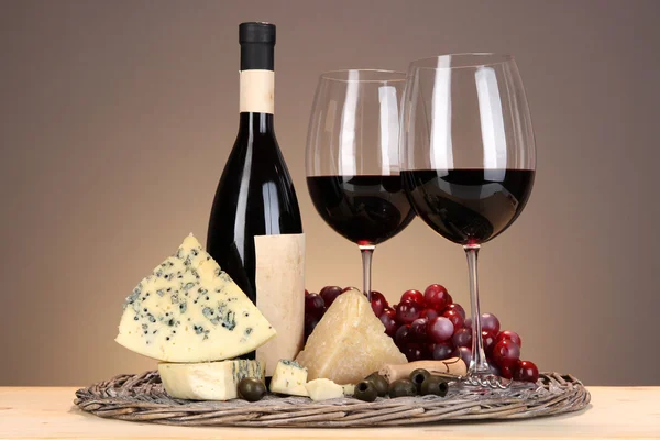 Refined still life of wine, cheese and grapes on wicker tray on wooden table on beige background — Stock Photo, Image