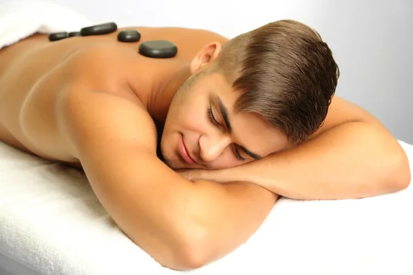 Young man relaxing with hot stones on back before massage — Stock Photo, Image