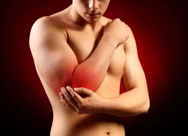 Junger Mann mit Ellbogenschmerzen, auf rotem Hintergrund — Stockfoto