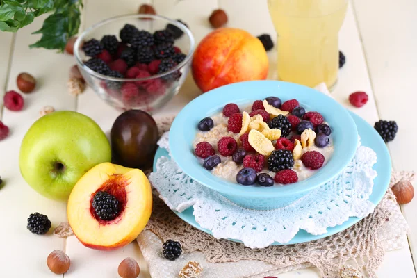 Oatmeal in plate with berries on napkins on wooden table on bright background — Stock Photo, Image