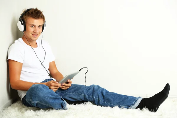 Young man relaxing on carpet and listening to music, on gray wall background — Stock Photo, Image