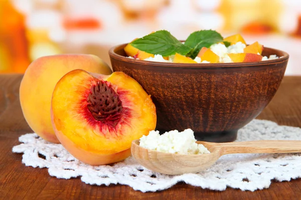 Sour cheese and pieces of fresh peach,on wooden table, on bright background — Stock Photo, Image