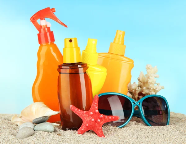 Garrafas com creme bronzeado e óculos de sol, sobre fundo azul — Fotografia de Stock