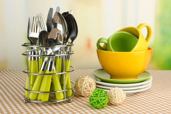 Cubertería de cocina en soporte de metal con platos limpios sobre mantel sobre fondo brillante — Foto de Stock