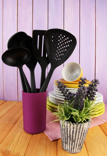 Utensilios de cocina de plástico en pie con platos limpios en la mesa sobre fondo de madera —  Fotos de Stock