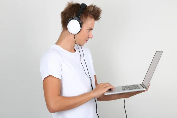 Schöner junger Mann hört Musik auf grauem Hintergrund — Stockfoto