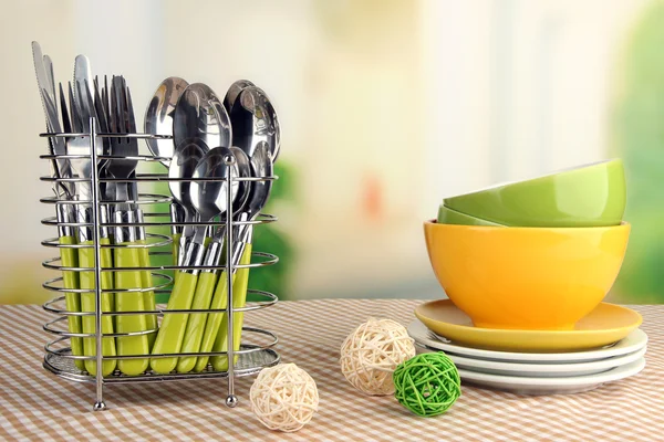 Posate da cucina in metallo stand con piatti puliti sulla tovaglia su sfondo luminoso — Foto Stock