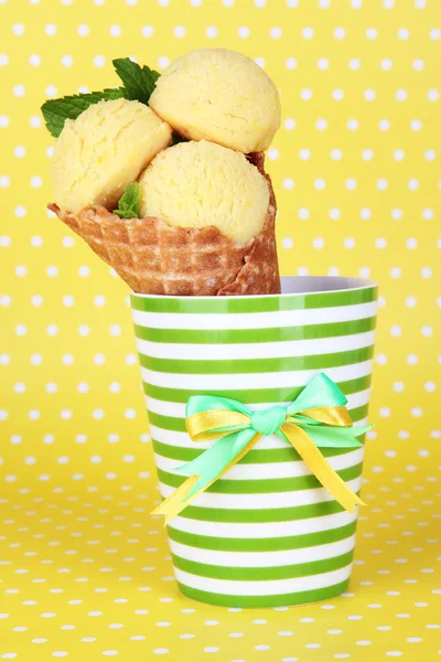 Appetitlich gelbes Eis mit Waffelkegel in Tasse auf gepunktetem Hintergrund — Stockfoto