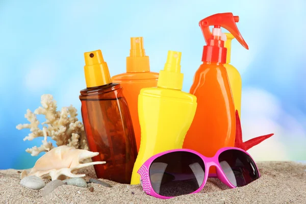 Bottiglie con crema abbronzante e occhiali da sole, su sfondo blu — Foto Stock
