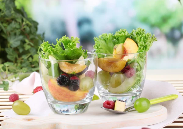 Salada de fruto em copos, em mesa de madeira, em fundo brilhante — Fotografia de Stock