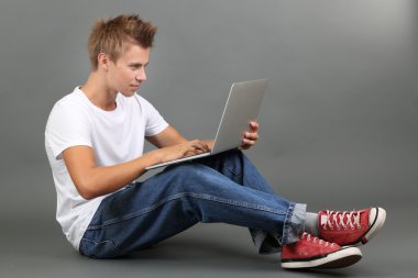 un joven guapo con portátil sobre fondo gris