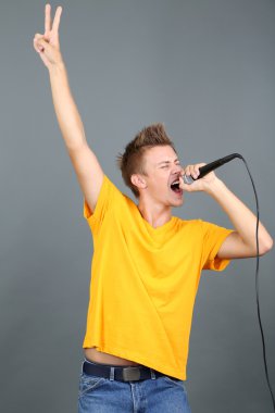 yakışıklı genç gri arka plan üzerinde şarkı söylüyor.