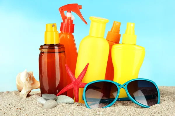 Botellas con crema bronceadora y gafas de sol, sobre fondo azul —  Fotos de Stock