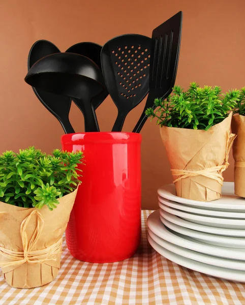 Utensílios de cozinha de plástico em stand com pratos limpos na toalha de mesa em fundo marrom — Fotografia de Stock