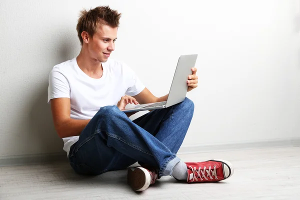 Un beau jeune homme avec ordinateur portable sur fond gris — Photo