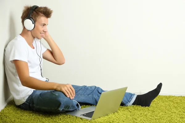 Jonge man ontspannen op tapijt en luisteren naar muziek, op grijze muur achtergrond — Stockfoto