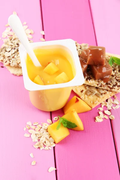 Läckra yoghurt med bitar av färsk frukt, kakor och flingor, på färg trä bakgrund — Stockfoto