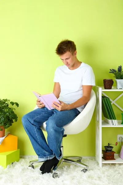 Jeune homme relaxant avec livre dans le fauteuil, sur le fond intérieur de la maison — Photo