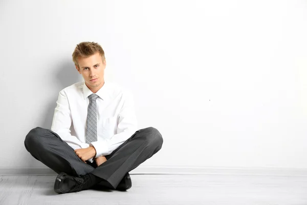 Молодой бизнесмен сидит на полу, на сером фоне стены — стоковое фото