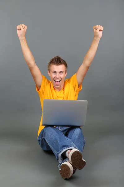 A handsome young man with laptop on grey background Stock Image
