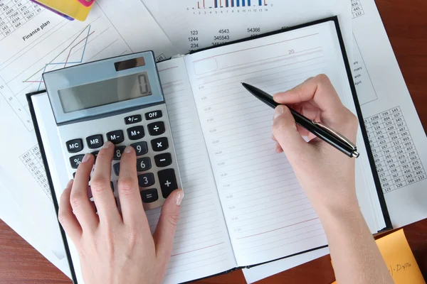 Mujer manos contando con calculadora en fondo de mesa de trabajo —  Fotos de Stock