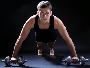 yakışıklı genç kaslı sporcu, koyu arka plan üzerinde egzersiz halter ile yürütmek