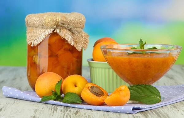 Apricot jam in glass jar and fresh apricots, on wooden table, on bright background — Stock Photo, Image