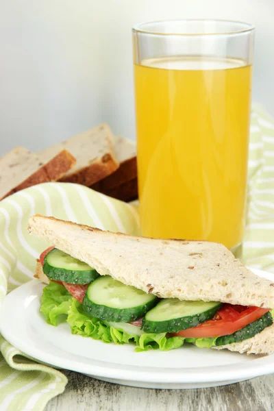 Compositie bij vruchtensap en lekkere sandwich met worst salami en groenten op kleur servet, op houten tafel, op lichte achtergrond — Stockfoto