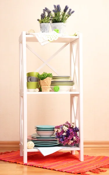 Prateleiras brancas bonitas com utensílios de mesa e decoração, no fundo da parede de cor — Fotografia de Stock
