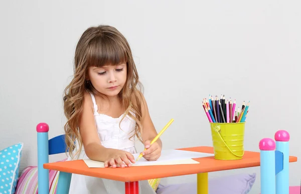 Petite fille dessine assis à table dans la chambre sur fond de mur gris — Photo