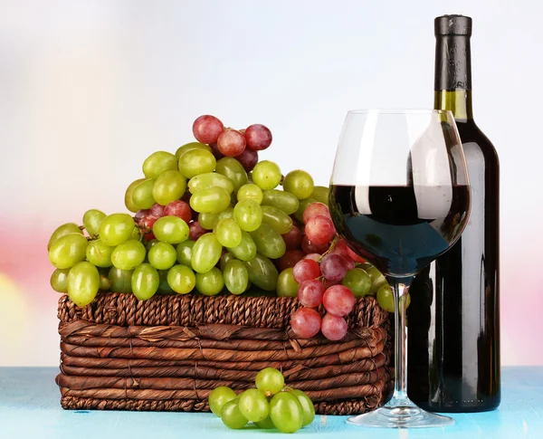 成熟的绿色和紫色葡萄与葡萄酒在明亮的背景上的木桌上的篮子里 — 图库照片