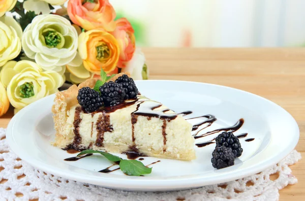 Scheibe Käsekuchen mit Schokoladensauce und Brombeere auf Teller, auf Holztisch, auf hellem Hintergrund — Stockfoto