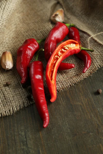 Chiles rojos picantes y ajo, sobre tela de saco, sobre fondo de madera — Foto de Stock