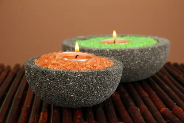 Свечи в каменных чашах с морской солью, на бамбуковом коврике, на коричневом фоне — стоковое фото
