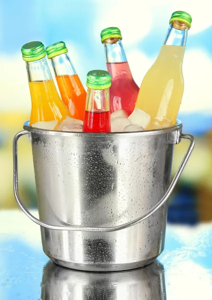 Botol dengan minuman lezat di ember dengan es batu, di latar belakang cerah — Stok Foto