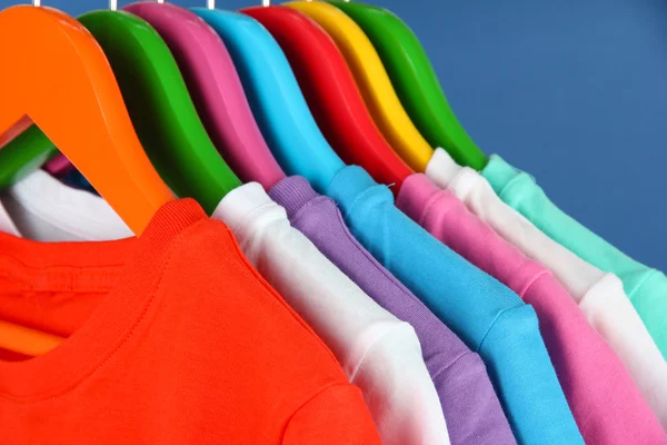 Camisas diferentes em cabides coloridos no fundo azul — Fotografia de Stock