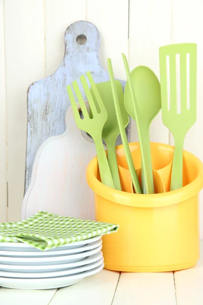 Utensílios de cozinha de plástico em copo na mesa de madeira — Fotografia de Stock