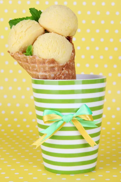Appetitlich gelbes Eis mit Waffelkegel in Tasse auf gepunktetem Hintergrund — Stockfoto