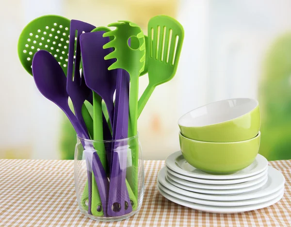 Plastic kitchen utensils in stand with clean dishes on tablecloth