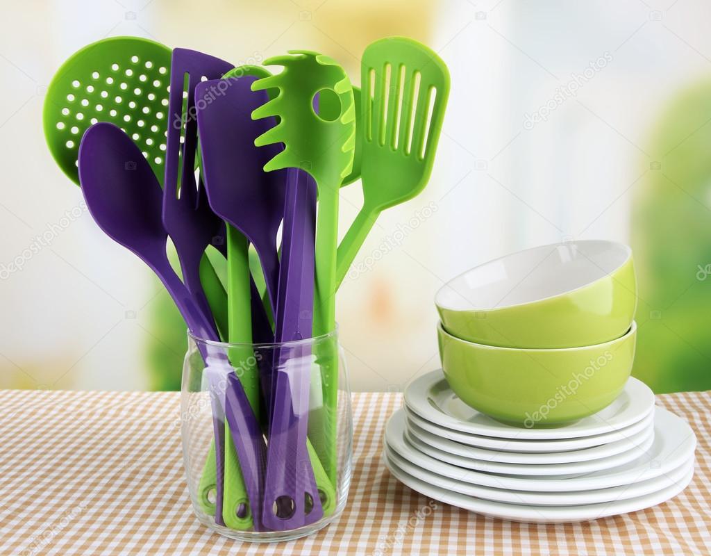 Plastic kitchen utensils in stand with clean dishes on tablecloth on bright  background Stock Photo by ©belchonock 32505067