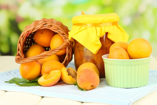 Confiture d'abricots dans un bocal en verre et abricots frais, sur table en bois, sur fond lumineux — Photo