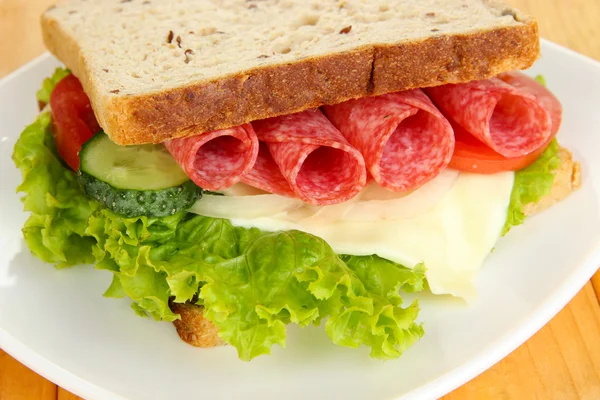 Sandwich savoureux avec saucisse de salami et légumes sur assiette blanche, sur fond de bois — Photo