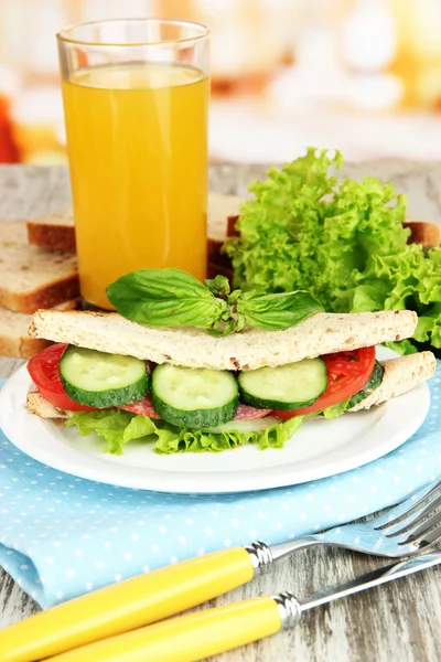 Composição com suco de frutas e saboroso sanduíche com salsicha de salame e legumes em guardanapo de cor, em fundo de mesa de madeira — Fotografia de Stock