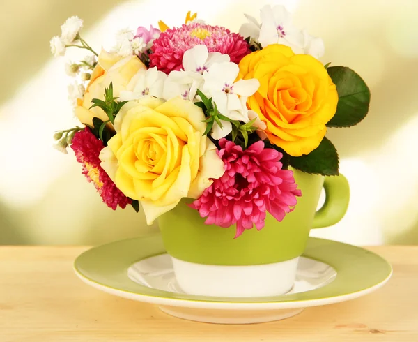 Beautiful bouquet of bright flowers in color mug, on wooden table, on bright background — Stock Photo, Image