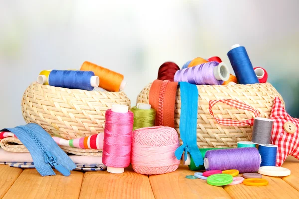 Paniers en osier avec accessoires pour la broderie sur table en bois, sur fond lumineux — Photo