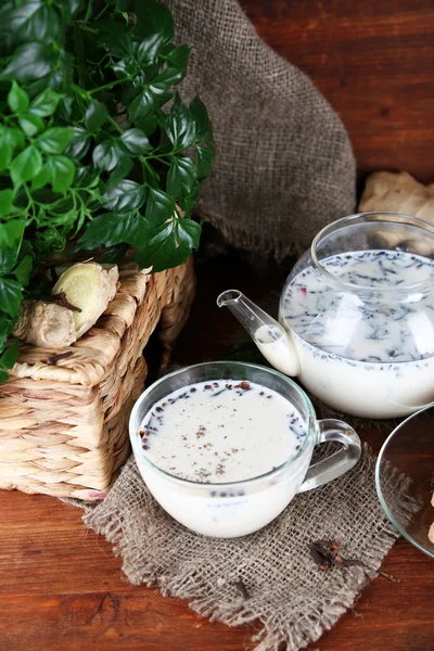 Tekanna och kopp te med mjölk och kryddor på säckväv av träbord på ljus bakgrund — Stockfoto