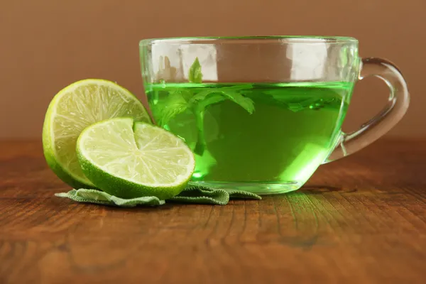 Transparent cup of green tea with lime and sage on table on brown background — Stock Photo, Image