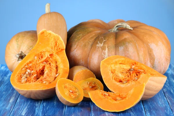 Rijp gesneden pompoenen op houten tafel op blauwe achtergrond — Stockfoto