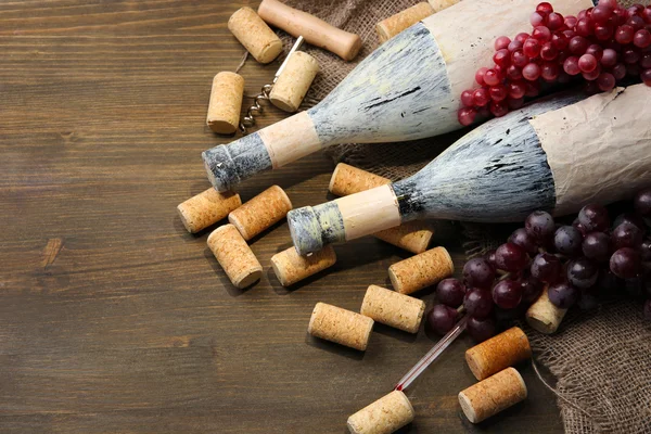 Old bottles of wine, grapes and corks on wooden background — Stock Photo, Image